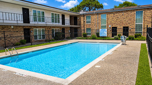 A swimming pool in front of a brick building with a sign that says "For Rent".
