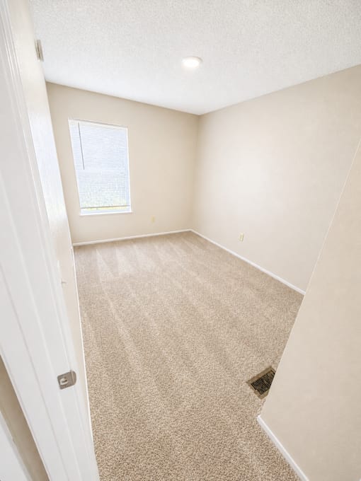 A room with a carpeted floor and a window with blinds.
