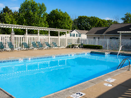 A blue swimming pool with a white fence and trees in the background.