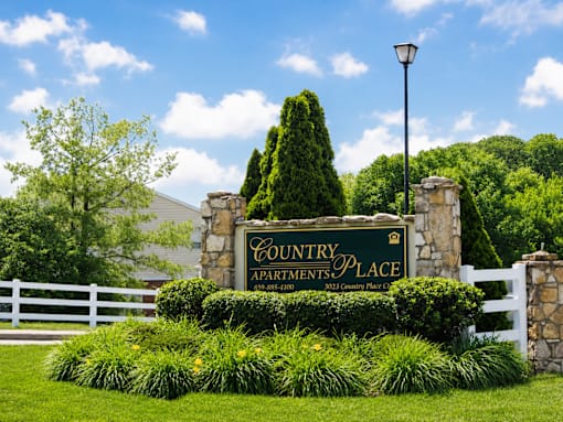 A sign for Country Apartments Place is surrounded by greenery.