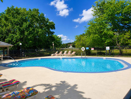 A pool surrounded by trees and chairs.