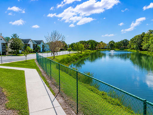 A serene park with a lake, a fence, and a walking path.