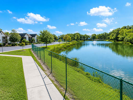 A serene lake surrounded by a green fence and a clear blue sky.