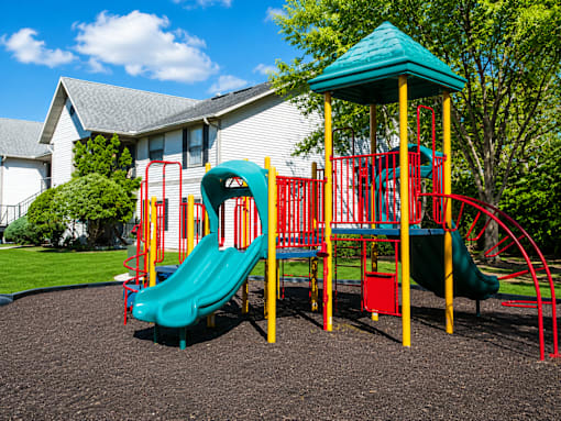 A playground with a green slide and red and yellow play structure.
