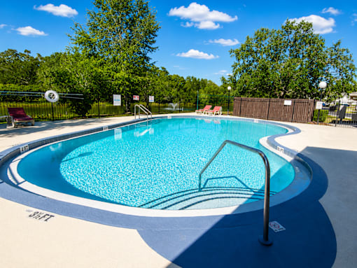A blue swimming pool surrounded by a black fence and trees.