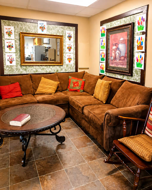 A living room with a brown couch, a round table, and a mirror on the wall.