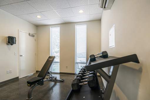 A gym room with a bench, weights, and a television.