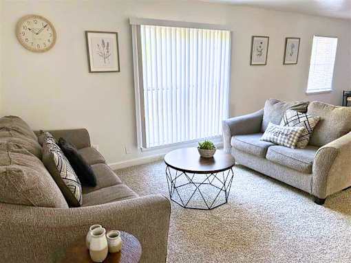A living room with a grey couch, a coffee table, and a clock on the wall.
