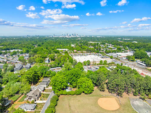 A bird's eye view of a residential area with a baseball field and a city skyline in the distance.