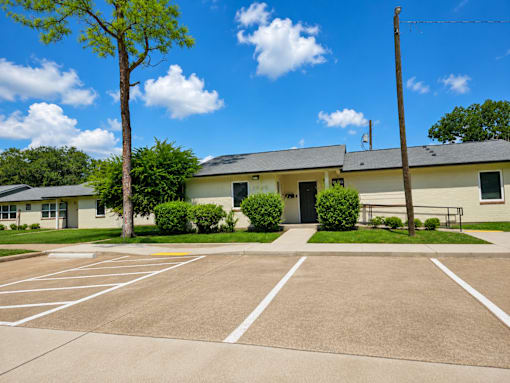 A parking lot in front of a building with a tree and bushes.