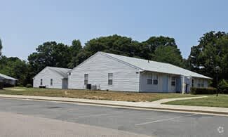 A white building with a grey roof is surrounded by a parking lot.