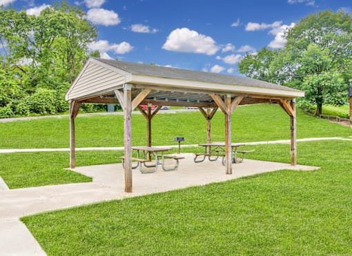 A wooden pavilion with picnic tables is surrounded by a grassy area.