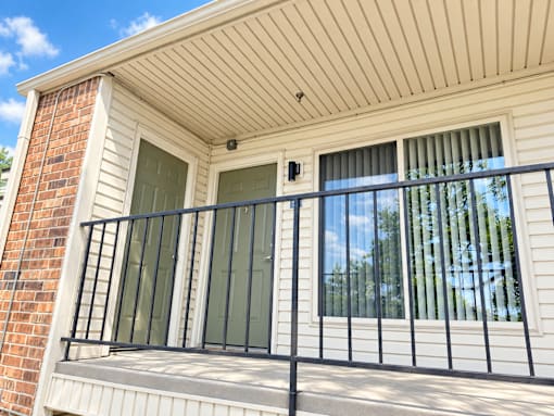A balcony with a black railing and a window with a view of trees.