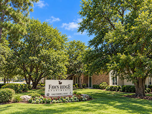 A sign for Fawn Ridge Apartments is in front of a building and trees.
