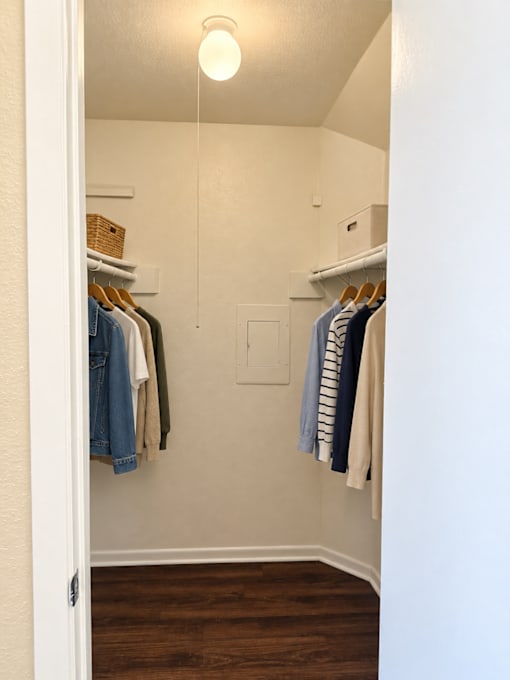 A white closet with clothes hanging on hangers.