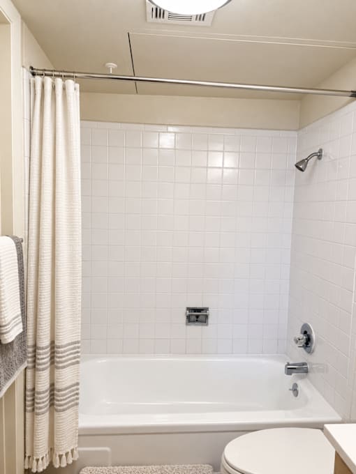 A white tiled bathroom with a white bathtub and toilet.