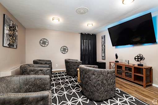 A living room with a large grey chair in the center and a flat screen TV mounted on the wall.