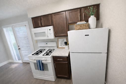 A white refrigerator stands in a kitchen with wooden cabinets and a white stove.