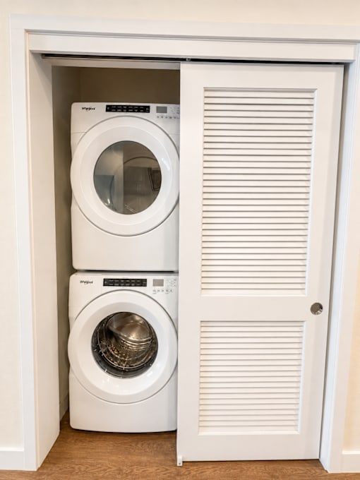 Two white washing machines are stacked in a white cabinet.