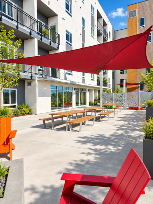 A red canopy is over a table and chairs outside a building.