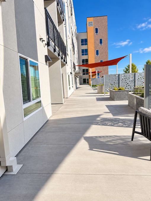 A long concrete walkway leads to a building with a red awning.