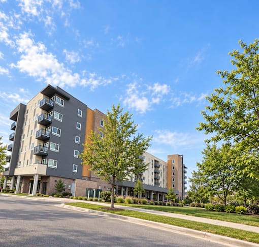 A modern apartment building with balconies and trees in front.