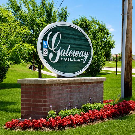 A sign that says Gateway Village in front of a green lawn.