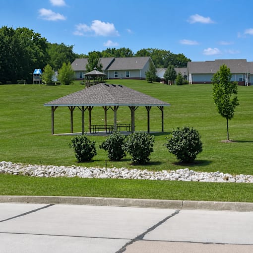 A gazebo is surrounded by bushes and trees in a grassy area.