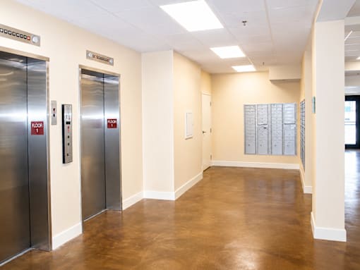 A hallway with two elevators on the left and a mailbox on the right.