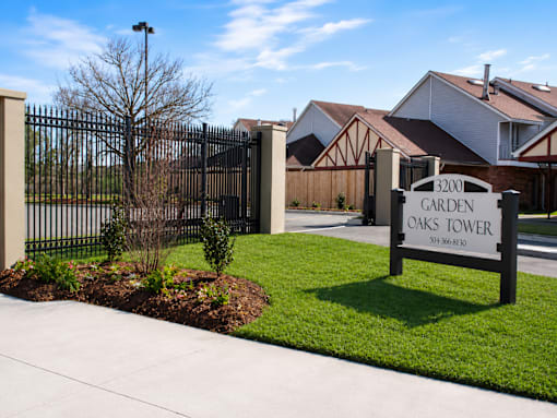 A sign for Garden Oaks Tower is in front of a black gate.