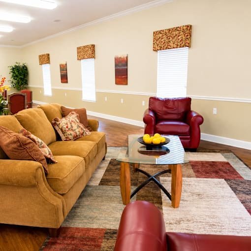 A living room with a yellow couch, a red chair, and a glass coffee table.