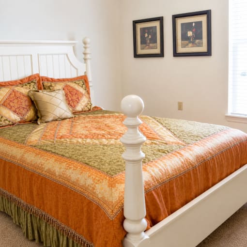 A bed with a white headboard and orange bedspread with a green and orange pillow.