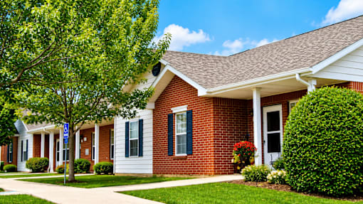 A red brick house with a white porch and a tree in front.