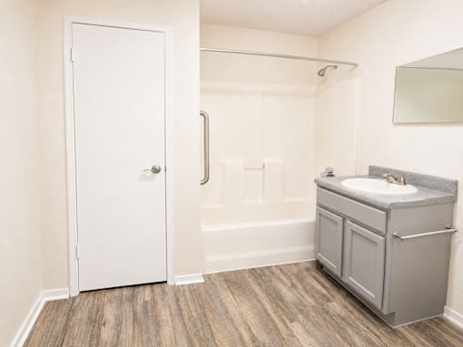 A white door is open to a bathroom with a sink and a wooden floor.