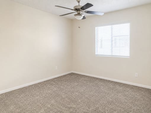A room with a ceiling fan and a window with blinds.