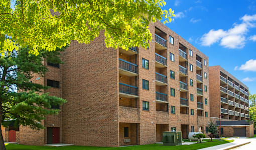 A large brick building with balconies and a tree in front.