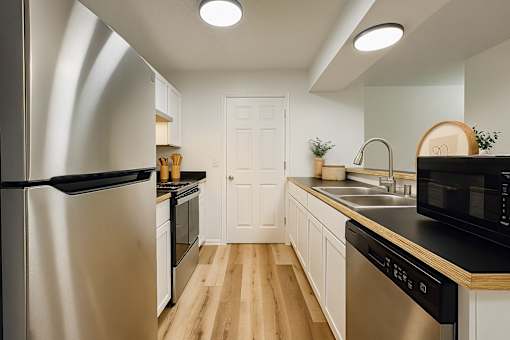 A modern kitchen with a stainless steel refrigerator and wooden flooring.
