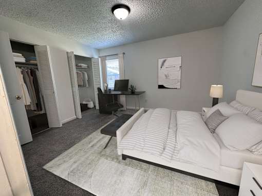 A bedroom with a bed, desk, and clothing rack.
