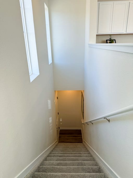a hallway with stairs and white walls and a door to a room with a staircase