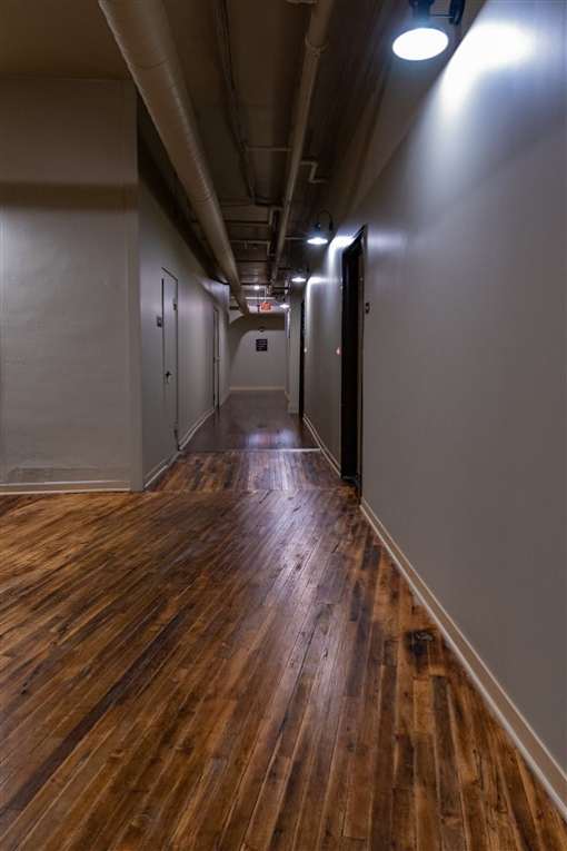 A long hallway with wood floors and metal pipes on the ceiling.