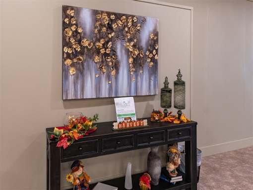 A painting of gold leaves hangs on a wall above a black table with a sign that says harvest.
