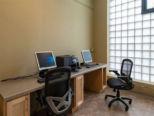 Two black chairs sit in front of a desk with two computers.