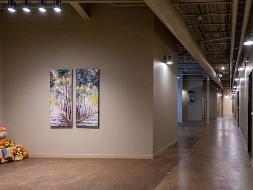 A long hallway with two paintings on the wall and a teddy bear on the floor.