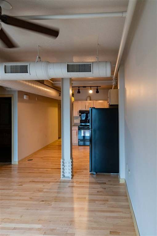 A room with a ceiling fan and a black refrigerator.