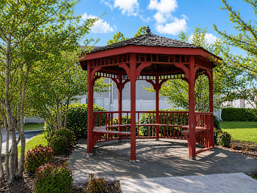A red gazebo is surrounded by trees and bushes.