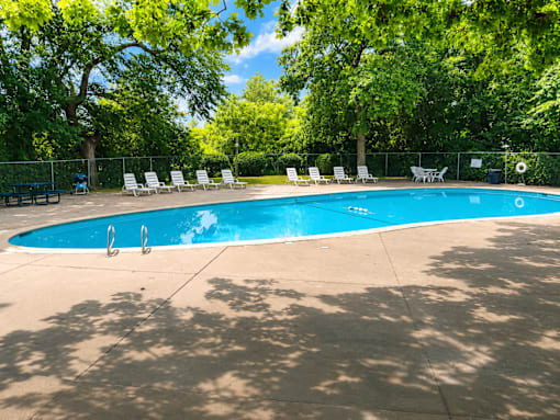 A swimming pool surrounded by trees and chairs.