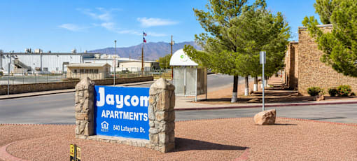 A sign for Jaycom Apartments stands in front of a building.