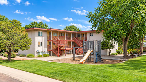 A playground with a slide is in front of a two-story building.