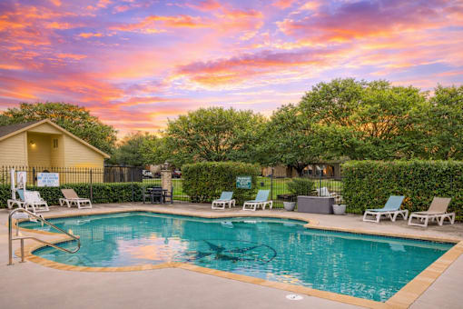 A pool surrounded by chairs and a house in the background.