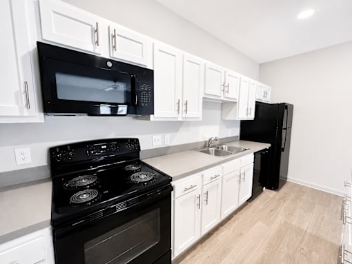 A black stove and microwave in a kitchen with white cabinets.